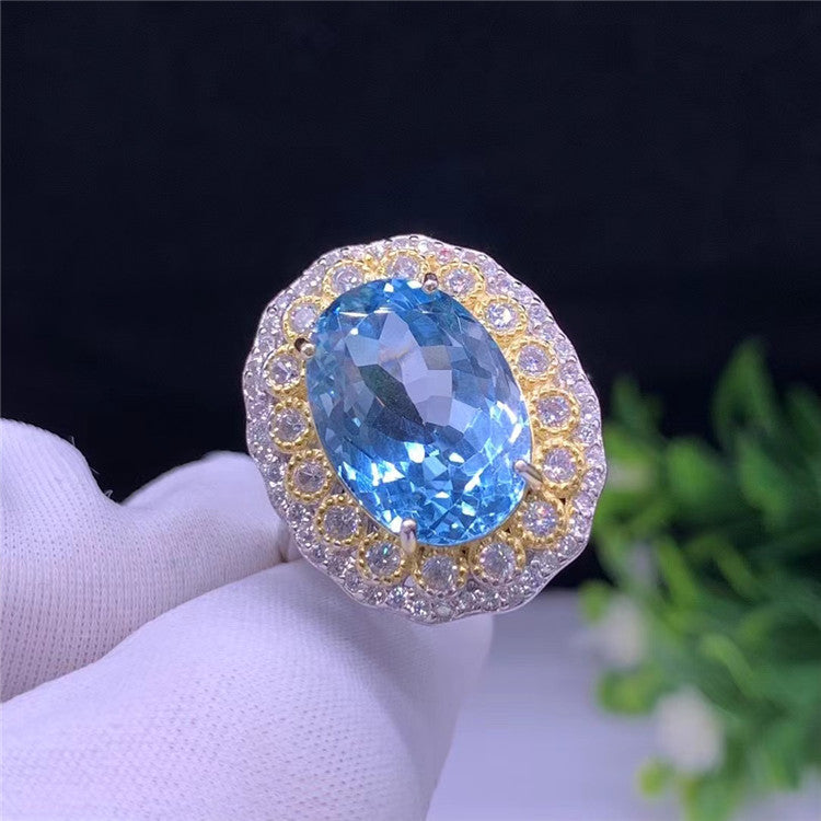 Ring with a blue gemstone held by a gloved hand against a dark background
