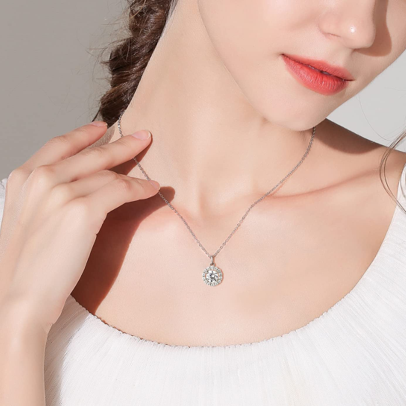 Woman wearing a silver necklace with a diamond pendant against a neutral background