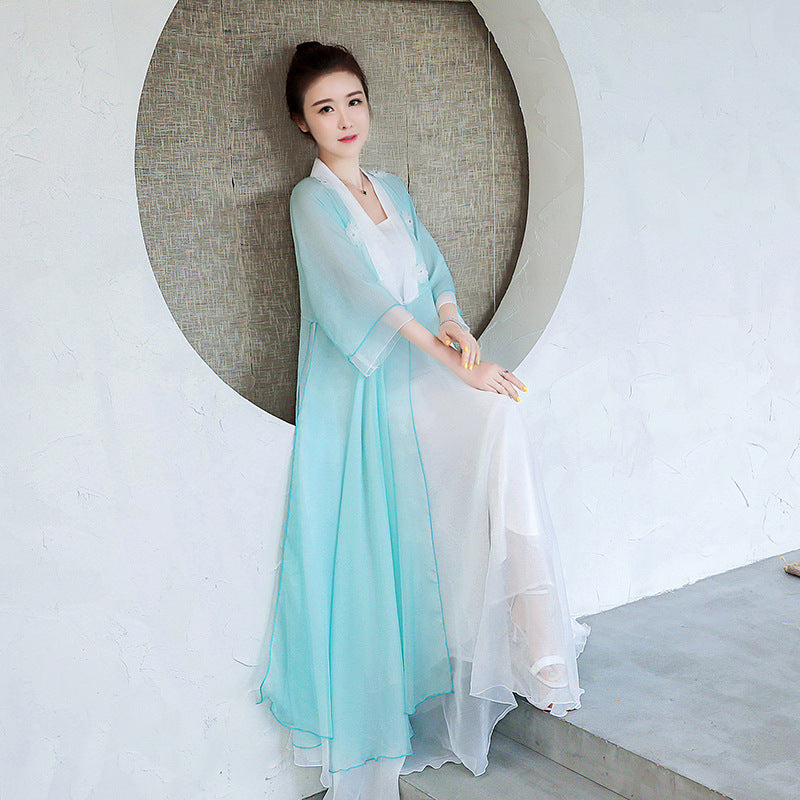 Woman in a light blue and white traditional outfit standing against a white wall with a circular design.